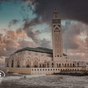 L'immagine mostra la Moschea di Hassan II a Casablanca, in Marocco, vicino all'Oceano Atlantico, con le nuvole e le onde che si infrangono contro la parete del mare, un vero Tesori del Marocco con il suo alto minareto che spicca.