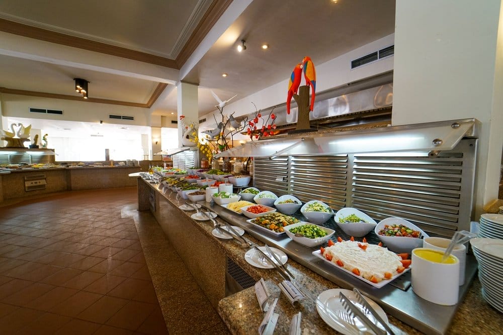 Il ristorante a buffet del Futura Club Brayka Bay presenta un lungo bancone con insalate, verdure e contorni assortiti in ciotole bianche. Sculture decorative di cibo e luci luminose arricchiscono l'ampia zona pranzo del resort.