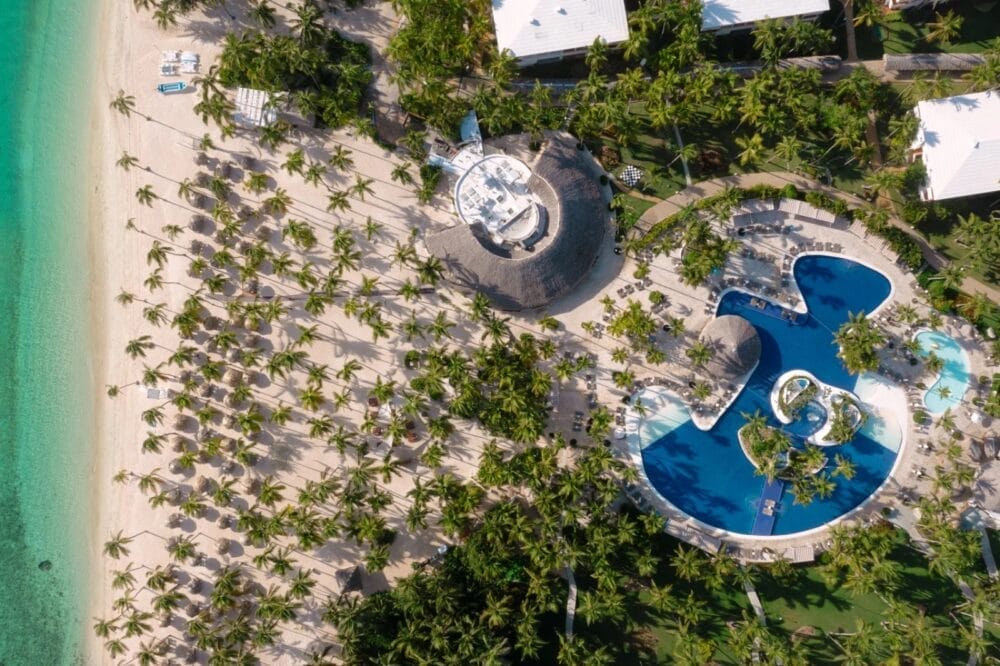 Vista aerea del Catalonia Bavaro a Bavaro Beach, caratterizzato da sabbia bianca, acqua turchese, molte palme, una grande piscina dalla forma unica ed edifici dai tetti bianchi circondati da una vegetazione lussureggiante.