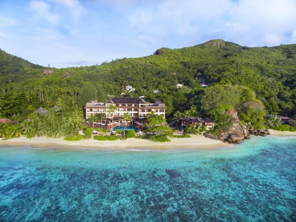 Vista aerea dell'Hilton Allamanda Resort, un rifugio sulla spiaggia immerso tra colline verdeggianti, con acque turchesi limpide, spiaggia sabbiosa e vegetazione tropicale nel cuore dell'Hilton Resort Seychelles.