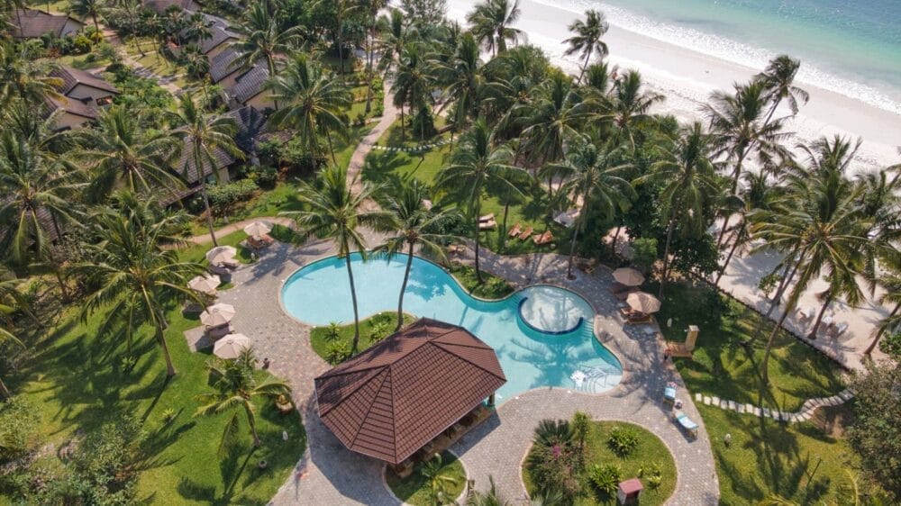 Vista aerea del Bravo Smart View Resort, un rifugio tropicale sulla spiaggia con palme, una grande piscina, lettini, ombrelloni e una spiaggia sabbiosa che si affaccia su acque turchesi sullo sfondo.