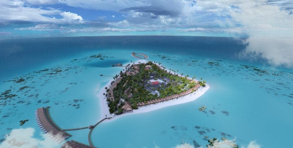 Veduta aerea di Brennia Kottefaru, un'isola di lusso delle Maldive, caratterizzata da una vegetazione lussureggiante, acque turchesi, bungalow overwater, barriere coralline e nuvole sparse sotto un cielo blu brillante.