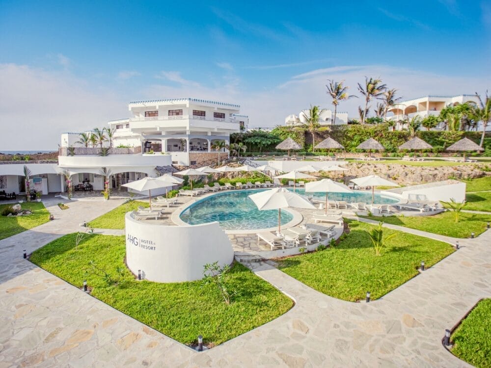 Sperimentate il lusso al Lion Beach Resort, un resort a 4 stelle con una grande piscina all'aperto, sedie a sdraio bianche e ombrelloni in mezzo a prati verdi e sentieri paesaggistici. L'edificio principale dell'hotel e le strutture con tetto di palapa attendono sotto un cielo blu.