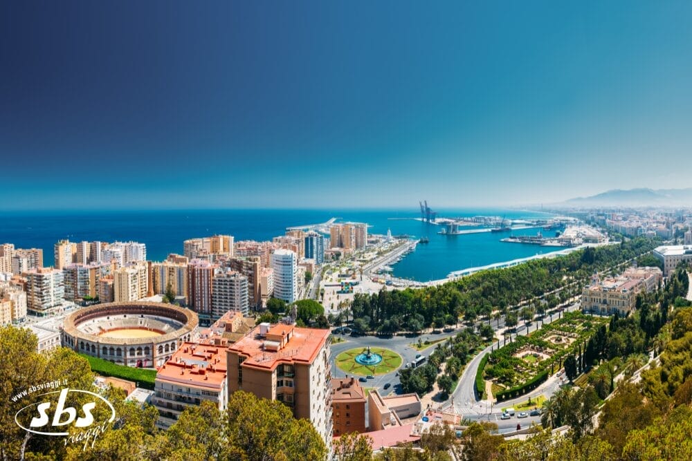Una vista panoramica di Malaga, parte del Gran Tour Andalusia, con l'arena dei tori, gli alti edifici, i parchi verdi e il porto affollato sotto un cielo azzurro e limpido, mentre il mare si estende in lontananza.
