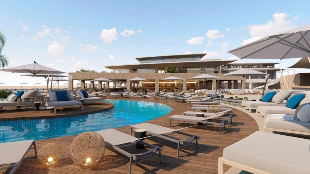 La lussuosa area piscina del Royal Horizon è caratterizzata da lettini, ombrelloni bianchi, cuscini e luci decorative su un ponte di legno. Il moderno edificio del resort si staglia sullo sfondo sotto un cielo blu con nuvole sparse.