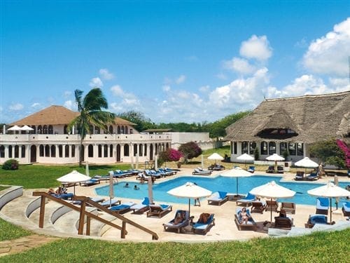Il Bravo Garoda Resort dispone di una piscina rotonda all'aperto circondata da lettini e ombrelloni, prati verdi, palme e due grandi edifici sotto un cielo blu con nuvole sparse. Gli ospiti si rilassano a bordo piscina in questo paradiso tropicale.