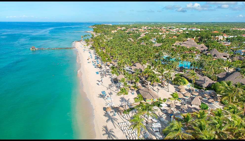Vista aerea di un resort tropicale con acqua turchese, sabbia bianca, palme e ombrelloni: il Catalonia Royal La Romana offre un esclusivo paradiso over 18 con una vegetazione lussureggiante e splendidi resort lungo la costa sotto un cielo per lo più sereno.
