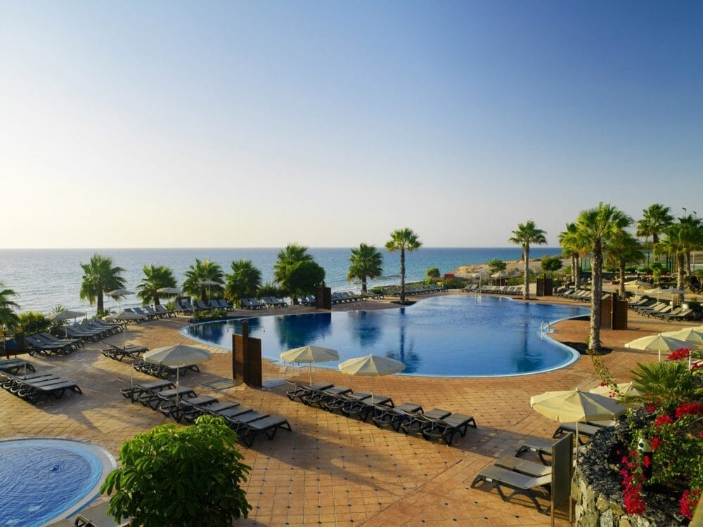 Al Veraclub Tindaya di Fuerteventura, l'area della piscina del resort è caratterizzata da sedie a sdraio, ombrelloni e palme con vista sull'oceano sotto un cielo azzurro e limpido. Godetevi il comfort all inclusive circondati da una vegetazione lussureggiante e da patii illuminati dal sole.