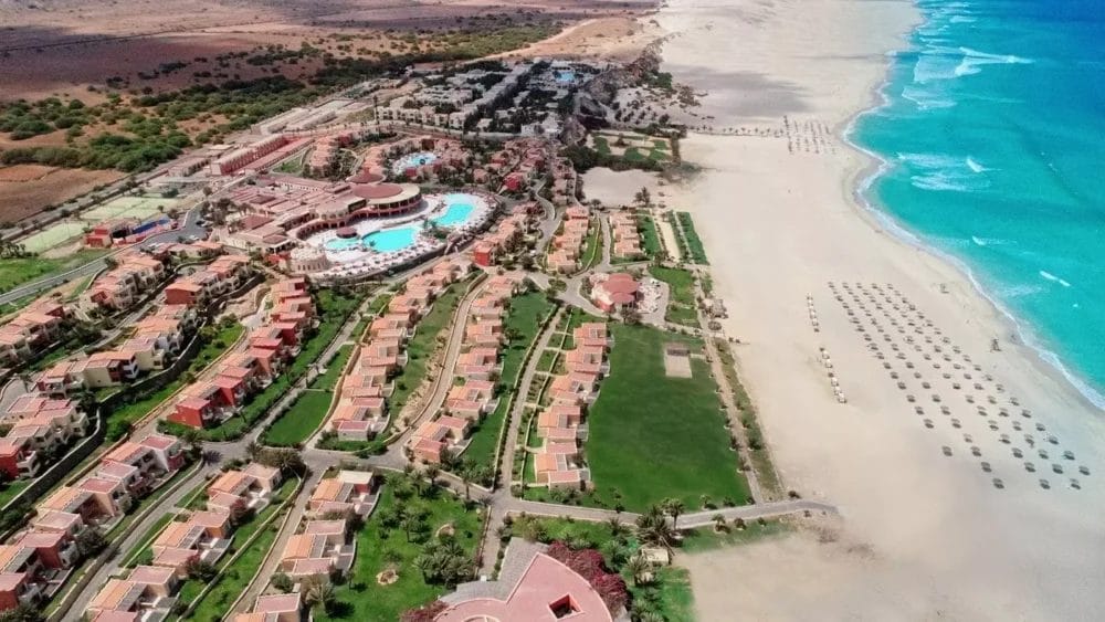 Vista aerea del resort Occidental Boa Vista con ville dai tetti rossi, grandi piscine e prati verdi accanto all'ampia spiaggia sabbiosa di Boa Vista Beach, con ombrelloni che costeggiano il mare blu turchese.