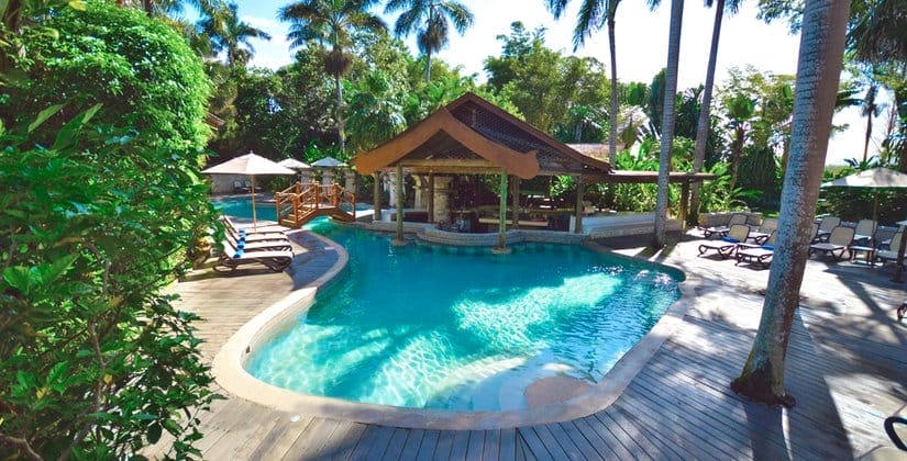 La piscina tropicale del Sunset At The Palms è circondata da palme, decking in legno, sedie a sdraio, ombrelloni e un bar con tetto in paglia. Il verde lussureggiante e la luce del sole creano un'atmosfera rilassante e invitante.