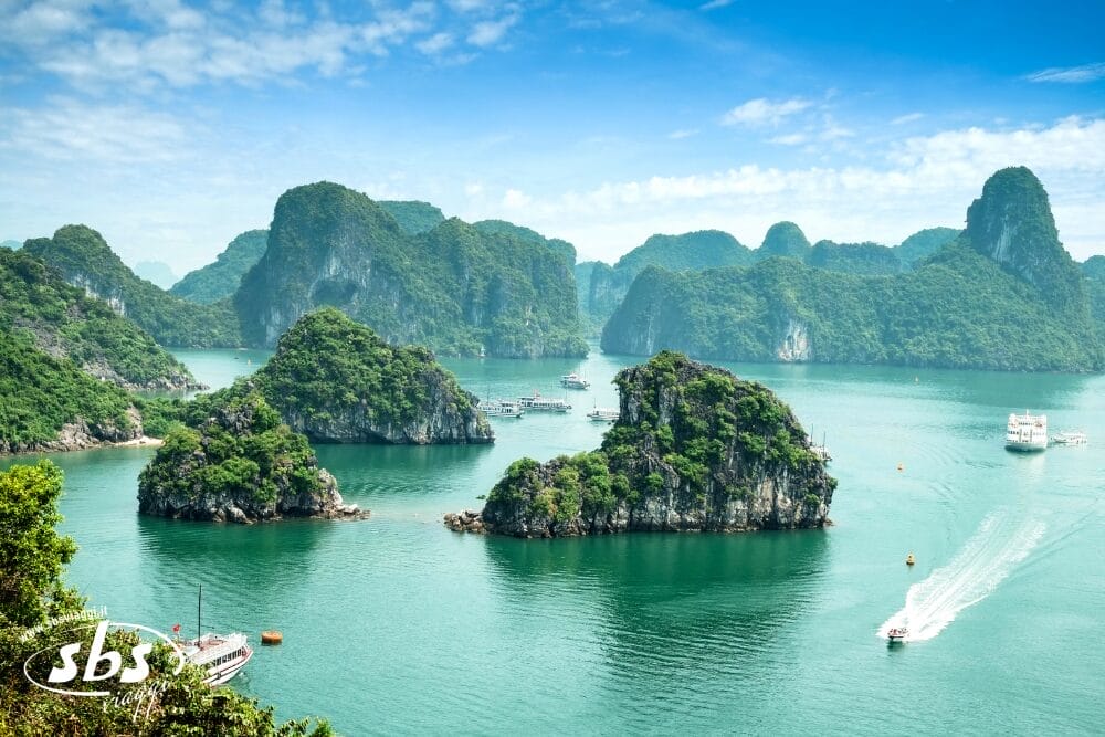 Vista panoramica dell'acqua verde smeraldo con isole calcaree e barche in crociera nella baia di Ha Long, in Vietnam. Bozza automatica esalta lo scenario, mentre il verde lussureggiante ricopre gli isolotti rocciosi sotto un cielo blu brillante.