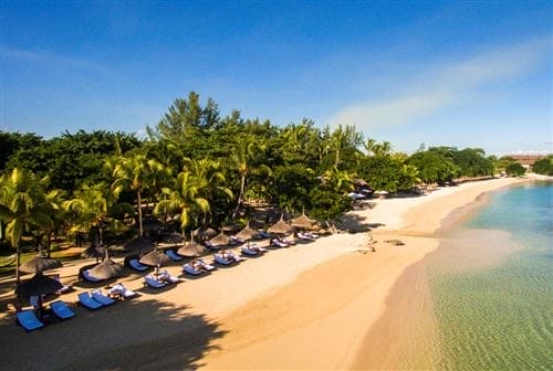 Una spiaggia tropicale con acque limpide e azzurre, fiancheggiata da palme e file di lettini con ombrelloni di paglia al Maritim Resort Mauritius, offre una fuga rilassante sull'arenile sotto un cielo luminoso e soleggiato.