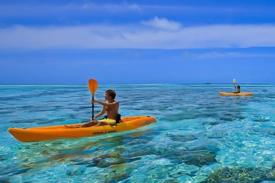 Due persone remano su kayak gialli in acque limpide e turchesi, sotto un cielo blu brillante. L'acqua è trasparente e rivela il corallo sotto la superficie. Entrambi i canoisti sembrano godersi la Bozza automatica di questo ambiente tranquillo e panoramico.