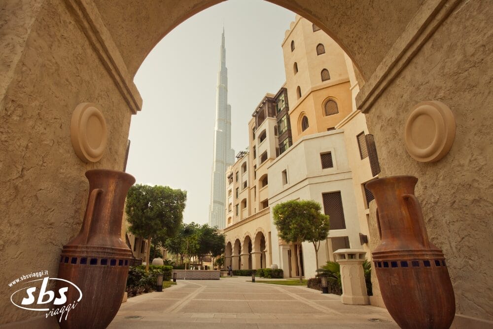 Una vista del Burj Khalifa di Dubai, incorniciato da un ingresso ad arco, con edifici beige in stile tradizionale, grandi vasi decorativi e verde in primo piano in una giornata limpida: un'esperienza perfetta di Minitour.