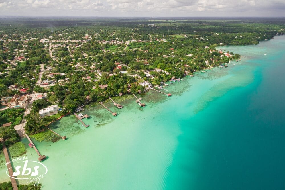 Veduta aerea di una città costiera di Tenerife con acqua turchese, alberi verdi, moli che si protendono nel mare e case sulla riva: uno scenario invitante per il vostro viaggio Capodanno sotto un cielo parzialmente nuvoloso.