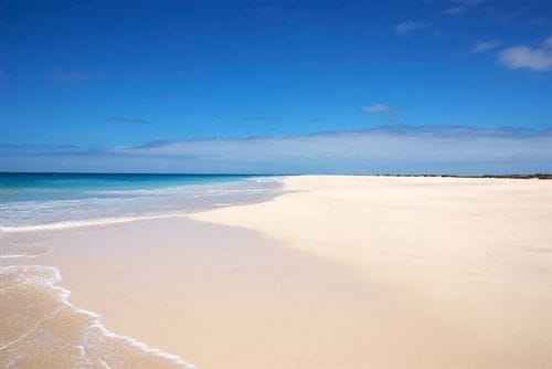 Un'ampia spiaggia sabbiosa e vuota vicino al Riu Cabo Verde è caratterizzata da onde dolci, acque turchesi e limpide e un cielo blu brillante con qualche nuvola.