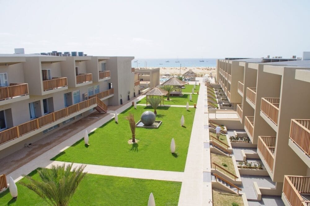 L'Oasis Salinas Sea, un moderno resort, presenta due edifici beige che si fronteggiano su un prato curato con palme, sculture decorative e sentieri. In lontananza si trova una piscina scintillante e una splendida vista sul mare.