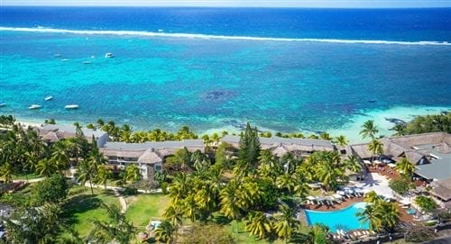 Vista aerea di Solana Beach, un resort tropicale sulla spiaggia con palme lussureggianti, piscina e lettini. L'oceano turchese si estende dietro il resort e le barche sono visibili nell'acqua cristallina.