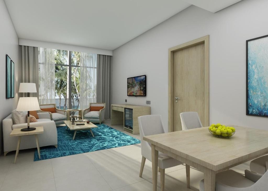 Soggiorno e sala da pranzo moderni e luminosi, con mobili in legno chiaro, pareti bianche, tappeto blu, ampie finestre con tende trasparenti, che richiamano lo stile fresco di un Beach Resort come il Centara Mirage. Una ciotola di mele verdi si trova sul tavolo da pranzo.