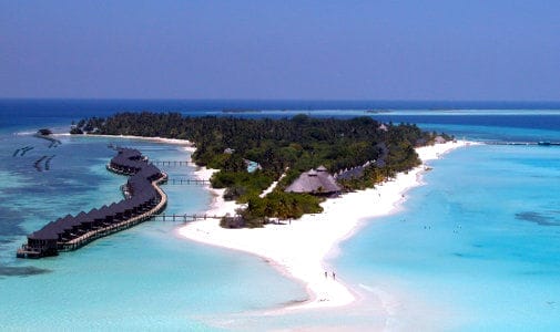 Veduta aerea del Kuredu Island Resort alle Maldive, che mostra le spiagge di sabbia bianca, l'acqua turchese, la vegetazione lussureggiante e i bungalow overwater che si estendono nel mare di questo resort di lusso.
