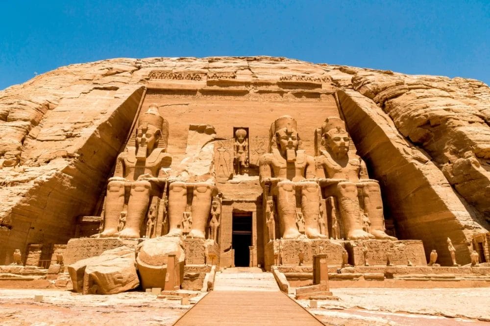 L'immagine mostra il Grande Tempio di Abu Simbel, in Egitto, con quattro grandi statue sedute del faraone Ramses II scolpite in una scogliera di arenaria, con un cielo azzurro e limpido sopra di esso: una tappa obbligata di ogni viaggio della Crociera Nefertari da Il Cairo.