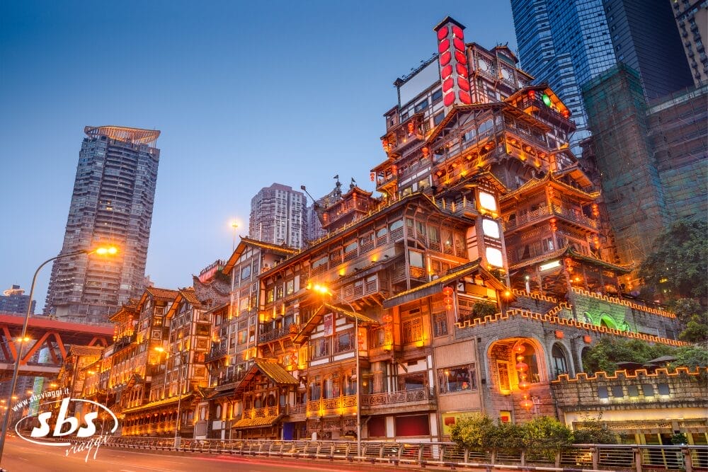 Un vivace edificio a più livelli con caratteristiche architettoniche tradizionali cinesi è illuminato al tramonto, circondato da moderni grattacieli in un paesaggio urbano: una vista iconica durante un Panda Tour alla scoperta dei Tesori del Sichuan. La strada di fronte è vuota.