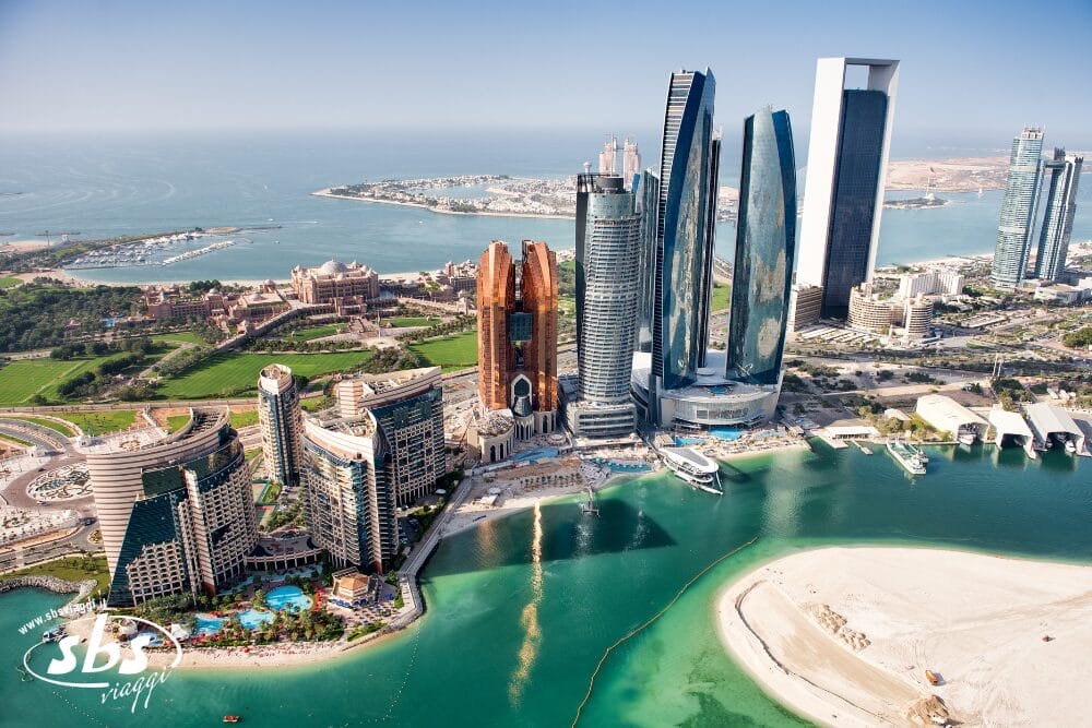 Veduta aerea dei moderni grattacieli sul lungomare di Abu Dhabi, che mostrano le meraviglie del turismo emiratino, con spazi verdi lussureggianti, piscine e spiagge sabbiose che circondano acque cristalline.