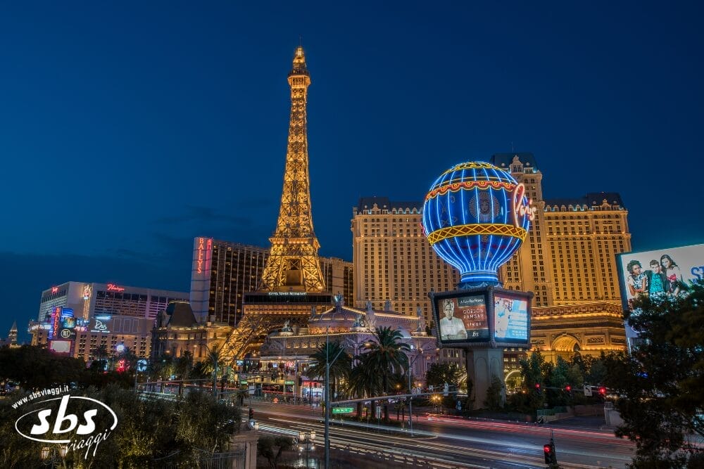 Vista notturna della Strip di Las Vegas con la replica illuminata della Torre Eiffel e dell'hotel Paris Las Vegas, con le scie luminose del traffico, i vivaci cartelloni pubblicitari e un'energia vivace che ricorda una notte di bozza automatica in città.