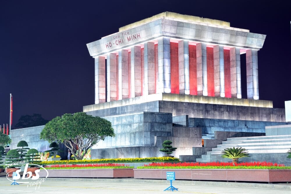 Il Mausoleo di Ho Chi Minh ad Hanoi, in Vietnam, illuminato di notte con luci rosse e bianche, circondato da alberi ben curati e aiuole colorate, offre uno spettacolo maestoso che ricorda un capolavoro di bozza automatica.
