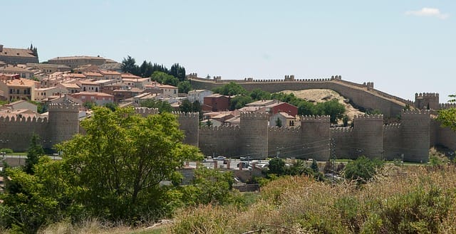Vista di una città storica con mura e torri in pietra, tetti in terracotta e aree erbose alberate che evocano un fascino senza tempo: una scena ispiratrice perfetta per la vostra prossima Bozza automatica sotto un cielo limpido.