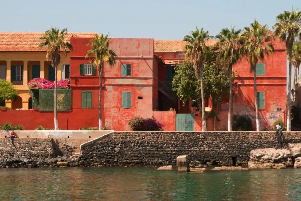 I colorati edifici in stile coloniale, dipinti di rosso e giallo con persiane verdi, si ergono dietro un muretto di pietra fiancheggiato da palme; i loro riflessi sull'acqua calma sotto un cielo limpido creano una scena che sembra un'automatica Bozza del paradiso.