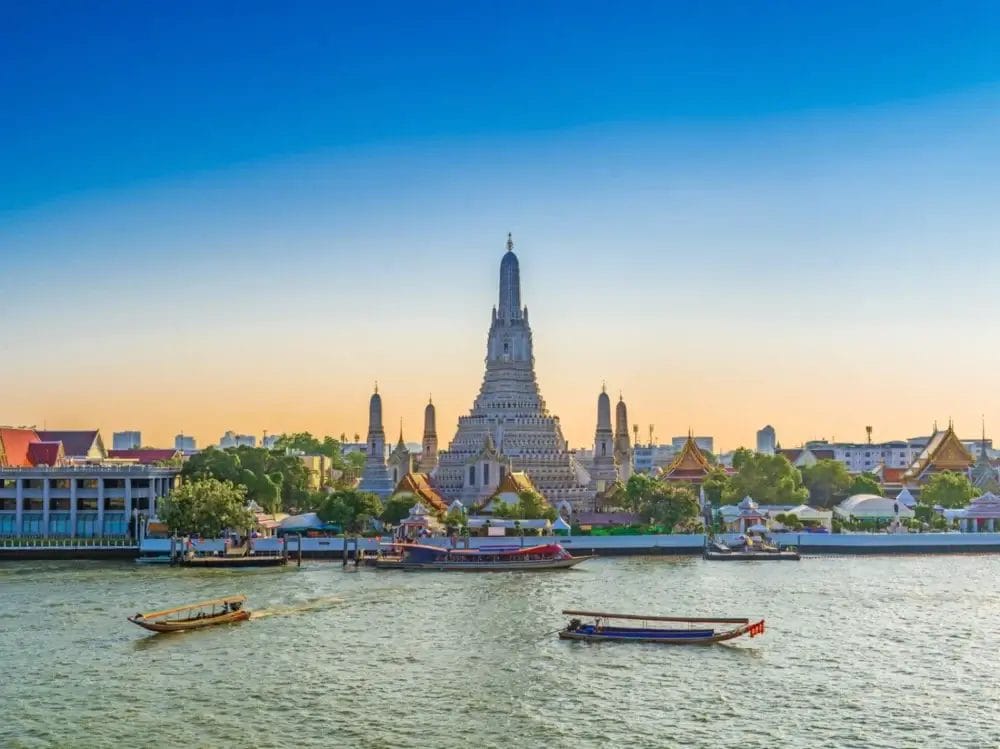 Una vista fluviale del tempio Wat Arun a Bangkok, in Thailandia, con le barche sul fiume Chao Phraya e un cielo limpido al tramonto, impreziosita dall'atmosfera serena di Bozza automatica.