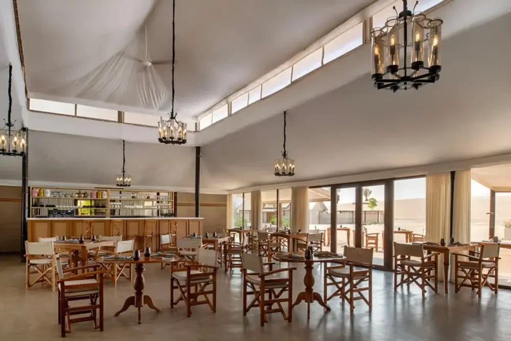 Ristorante spazioso e luminoso con tavoli e sedie in legno, ampie finestre, soffitto alto con tessuto drappeggiato, lampadari moderni e un'area bar sul retro. Godetevi il paesaggio esterno attraverso le finestre in questo elegante ambiente di Bozza automatica.