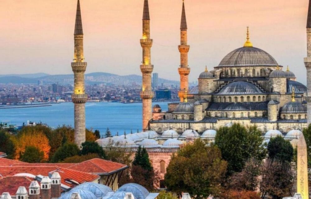 La Moschea Blu di Istanbul, con le sue cupole e i suoi minareti, è vista al tramonto con vista sullo stretto del Bosforo, come una Bozza automatica che cattura l'armonioso paesaggio urbano, incorniciato da alberi e tetti in primo piano.