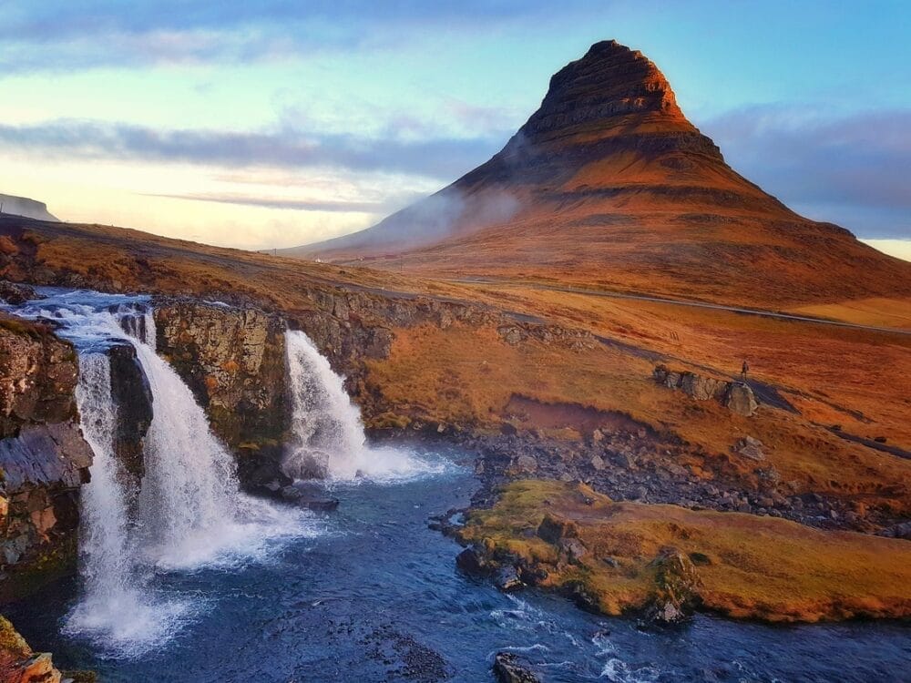 Una vista panoramica del monte Kirkjufell in Islanda all'alba, con una cascata che sfocia in un fiume in primo piano e la luce dorata che illumina il paesaggio, crea una bozza naturale automatica di bellezza e tranquillità.