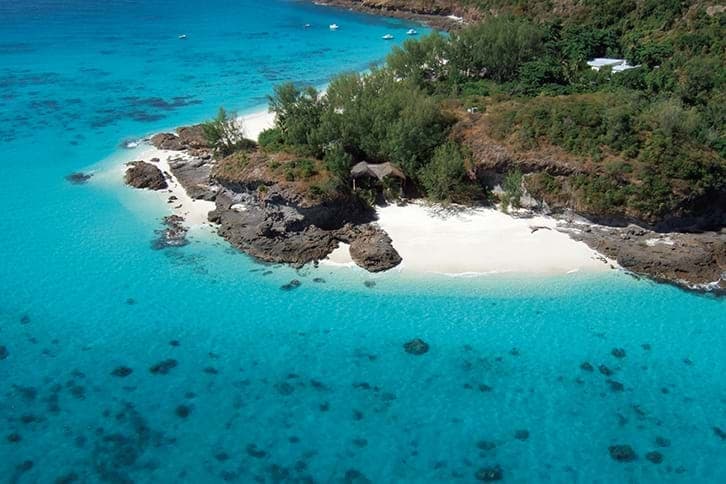 Vista aerea del Constance Tsarabanjina, un resort di lusso sull'isola del Madagascar, caratterizzato da una vegetazione lussureggiante, da una spiaggia di sabbia bianca, da un litorale roccioso e da un'acqua limpida e turchese circondata da barriere coralline.