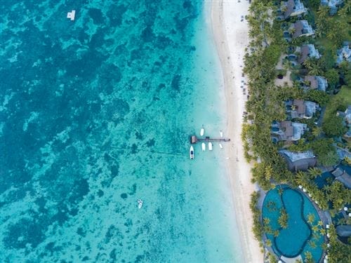 Veduta aerea di Trou Aux Biches con acqua turchese, spiaggia sabbiosa, piccole imbarcazioni al molo ed edifici del resort Beachcomber circondati da palme e piscina.