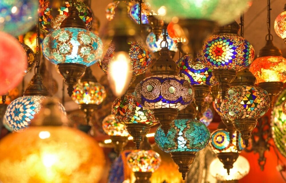 Una varietà di lanterne in vetro a mosaico colorato con motivi intricati sono appese a stretto contatto, creando un'esposizione di luce calda, vibrante e artistica: un'incantevole bozza automatica di colori e design.