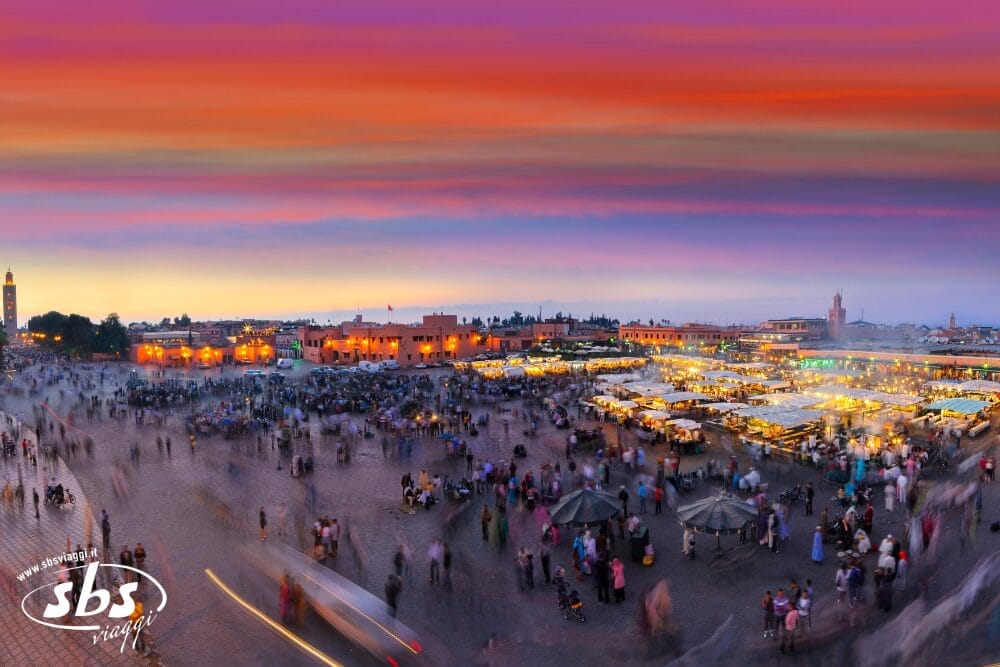 Una vibrante piazza del mercato al tramonto, piena di folla e di bancarelle di cibo sotto un cielo colorato, con gli edifici storici illuminati sullo sfondo, cattura l'essenza vivace di Bozza automatica.