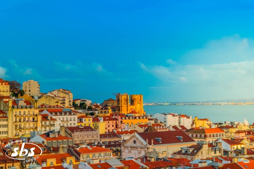 Tetti colorati ed edifici storici di Lisbona, Portogallo, con il fiume Tago e il cielo azzurro sullo sfondo. Una chiesa e alcune case color pastello aggiungono fascino a questo paesaggio urbano automatico.