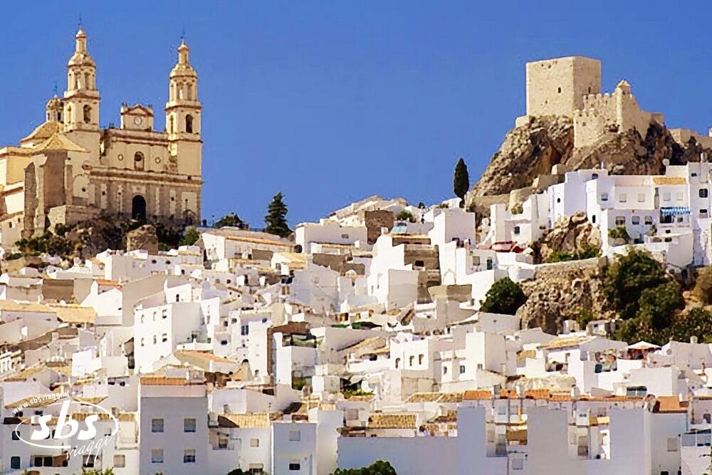 Un paese collinare con case bianche, una grande chiesa con torri gemelle sulla sinistra e un castello di pietra in cima alla collina sotto un cielo azzurro e limpido: un'idilliaca scena di Bozza automatica.