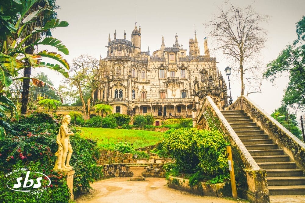 Un castello grandioso e ornato, dall'architettura gotica, si erge dietro giardini lussureggianti, una scalinata in pietra e una statua classica di nudo. Alberi alti e verdi circondano la scena, come se fossero stati creati da una bozza automatica, creando un'atmosfera fiabesca.