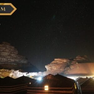 Veduta notturna di scogliere rocciose del deserto sotto un cielo stellato, con tetti di tende e luci soffuse in primo piano. Nell'angolo superiore sinistro compaiono le diciture "PREMIUM", "sbs viaggi" e una sottile filigrana Bozza automatica.