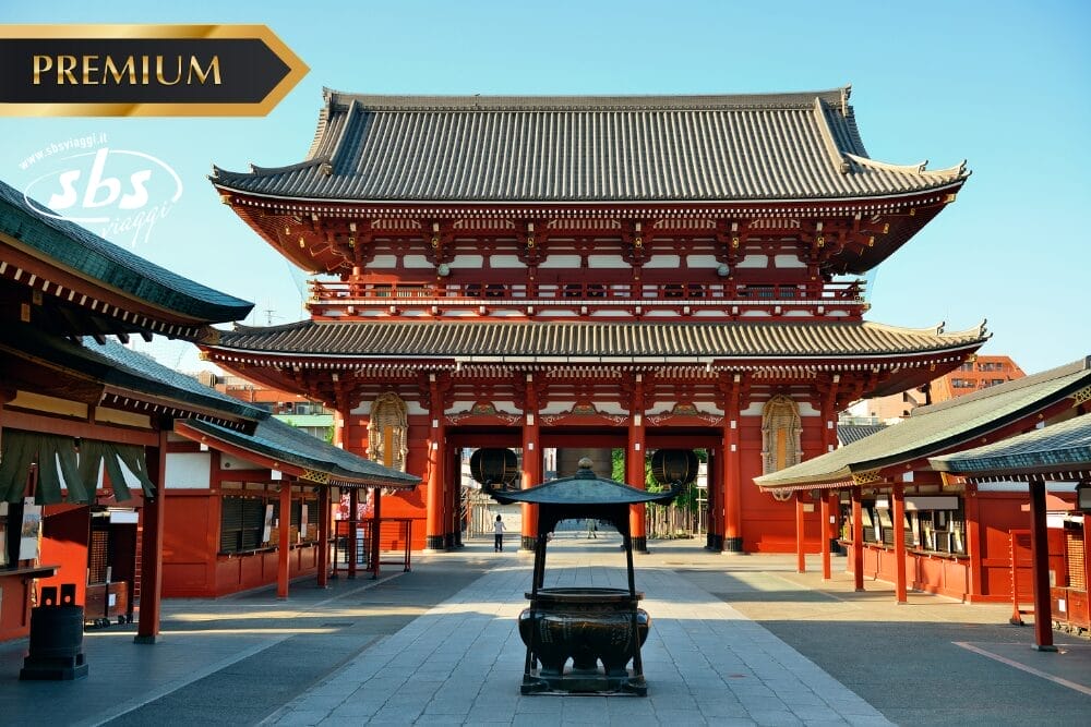 Un grande tempio giapponese tradizionale con colonne rosse e tetto ornato, visto dal cortile anteriore sotto un cielo azzurro. I loghi "Bozza automatica", "PREMIUM" e "sbs" appaiono negli angoli superiori dell'immagine.