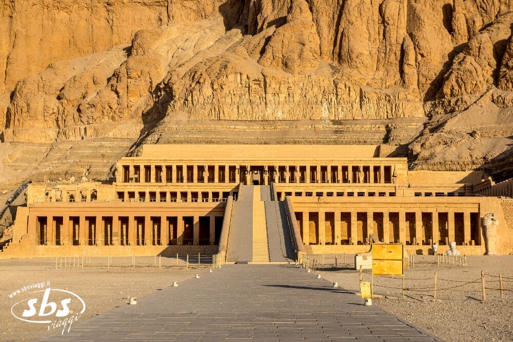 L'immagine mostra l'antico tempio mortuario di Hatshepsut in Egitto, costruito in una scogliera rocciosa con grandiose terrazze, pilastri e una scalinata centrale - quasi una bozza automatica - che emerge dal paesaggio desertico circostante.