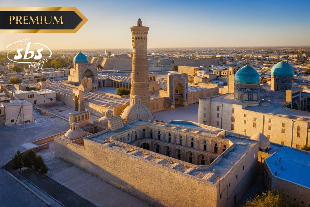 Vista aerea di edifici storici con cupole e minareti a Bukhara, in Uzbekistan, al tramonto. I loghi Premium e SBS Journey appaiono sull'immagine, esaltati da un sottile effetto di bozza automatica.