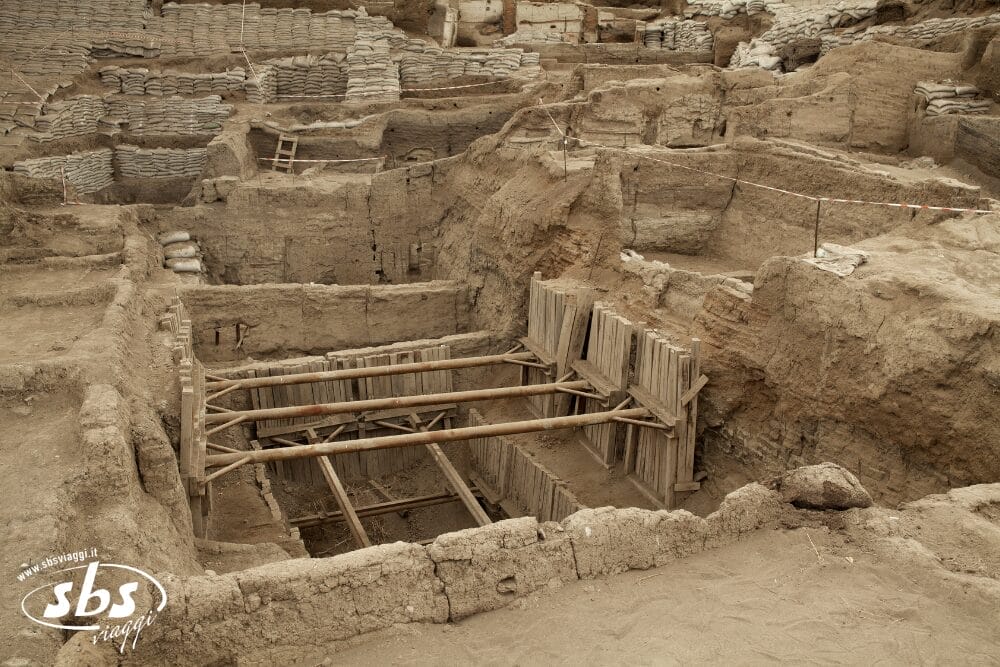 Un sito di scavo archeologico a Bodrum con profonde fosse rettangolari, sostenute da travi e assi di legno. L'area è circondata da muri di terra e sacchi di sabbia, contrassegnati da nastro rosso e bianco: una tappa classica del Tour Turchese.