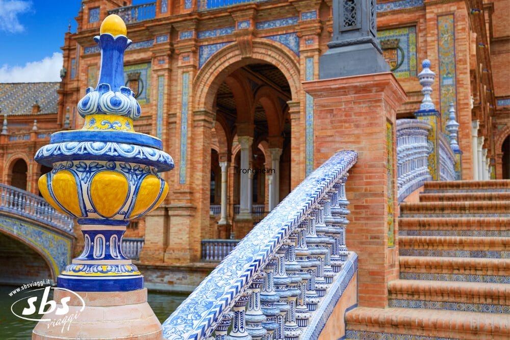 Ringhiera in piastrelle di ceramica colorate e palo decorativo su una scala di Plaza de España a Siviglia, in Spagna, con archi in mattoni dettagliati e motivi ornamentali sullo sfondo: un esempio ispiratore della maestria di Bozza automatica.