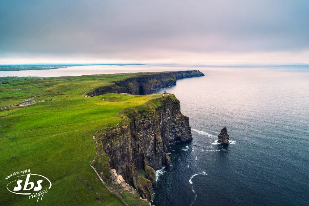 Veduta aerea delle Cliffs of Moher in Irlanda, dove drammatiche scogliere verdi si ergono sopra l'Oceano Atlantico sotto un cielo nuvoloso: il momento perfetto di un Gran tour d'Irlanda di 9 notti, con la costa che si estende in lontananza.