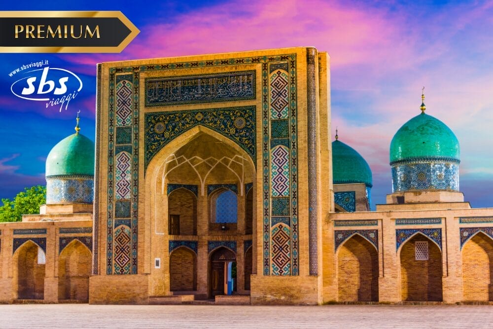 Moschea ornata con cupole blu e intricate piastrelle, sullo sfondo di un vibrante cielo al tramonto. La scritta "Premium" è riportata in un banner dorato in alto a sinistra, mentre il logo di viaggio "sbs viaggi" e la targhetta Bozza automatica compaiono sull'immagine.